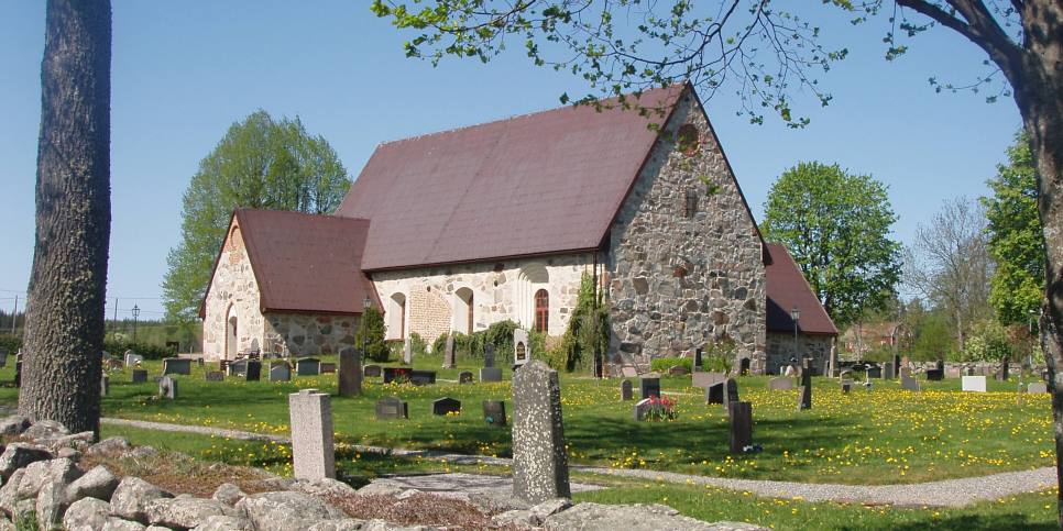 Frösunda kyrka med kyrkogård och gröna träd i bakgrunden.   