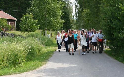 Pilgrimsvandrare längs en väg omgiven av sommargrönska