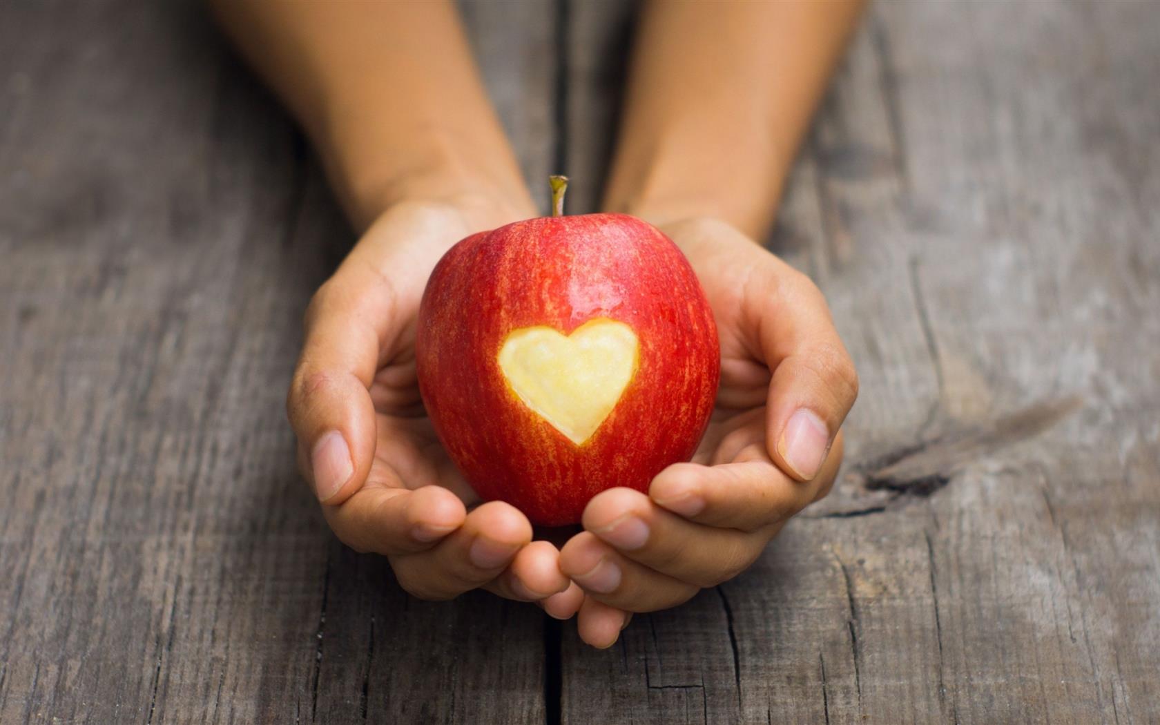 Kupade händer med ett äpple med hjärtformat tuggavtryck.