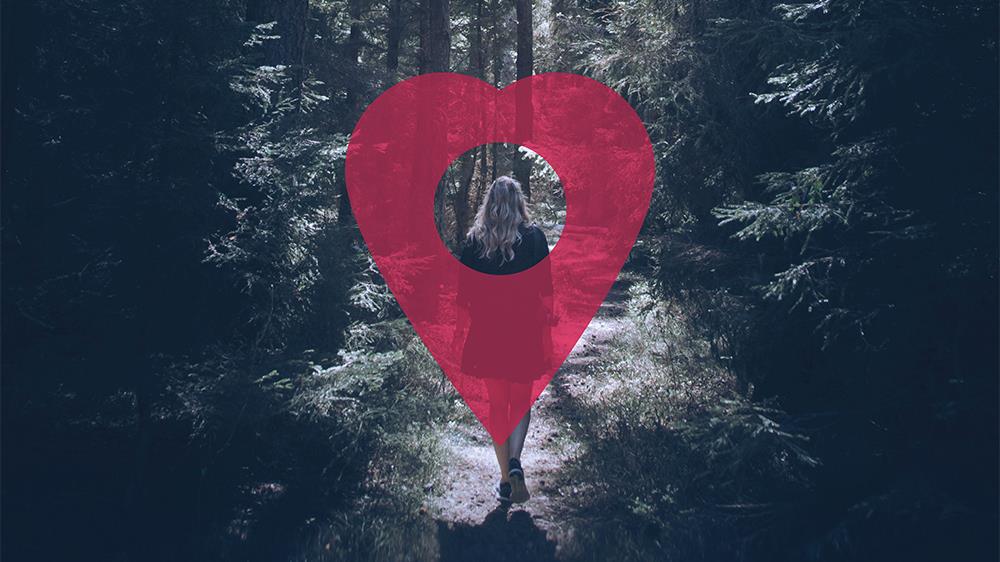 En kvinna går i en skog, ovanpå henne är en kartnål formad som ett hjärta.