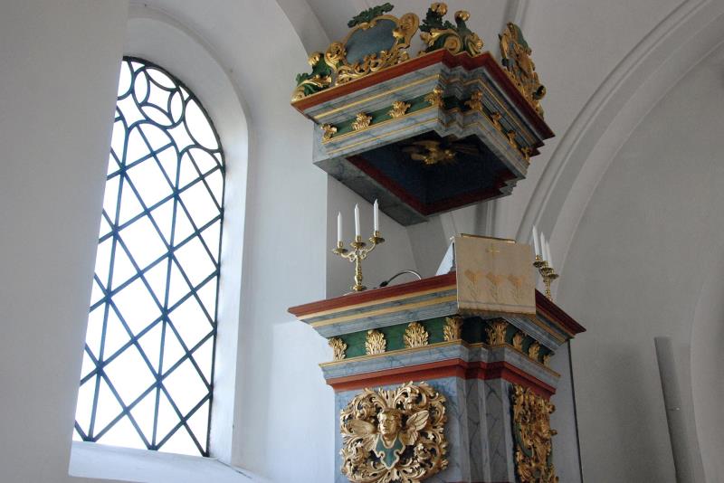 Predikstolen i Sövestad kyrka är målad i guld, grönt, grått och blått och är rikt dekorerad med bland annat kerubansikten och blomsterdekorationer.