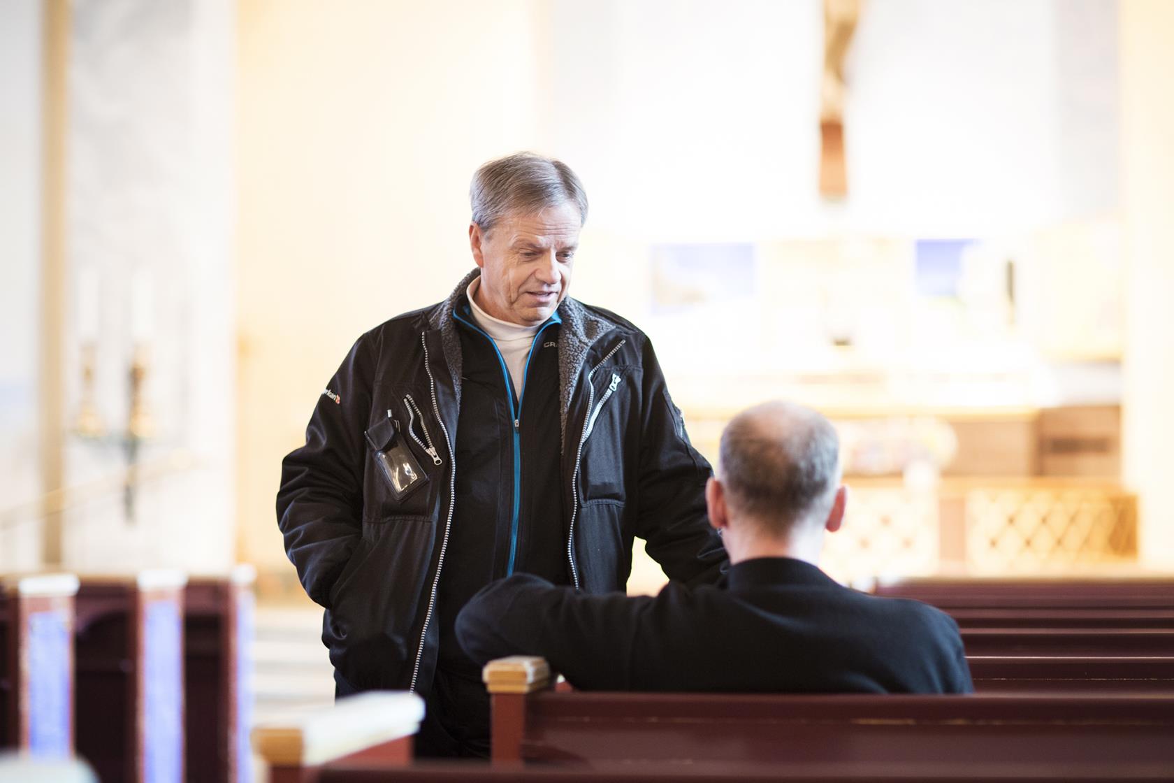 Två män samtalar i kyrkbänken.