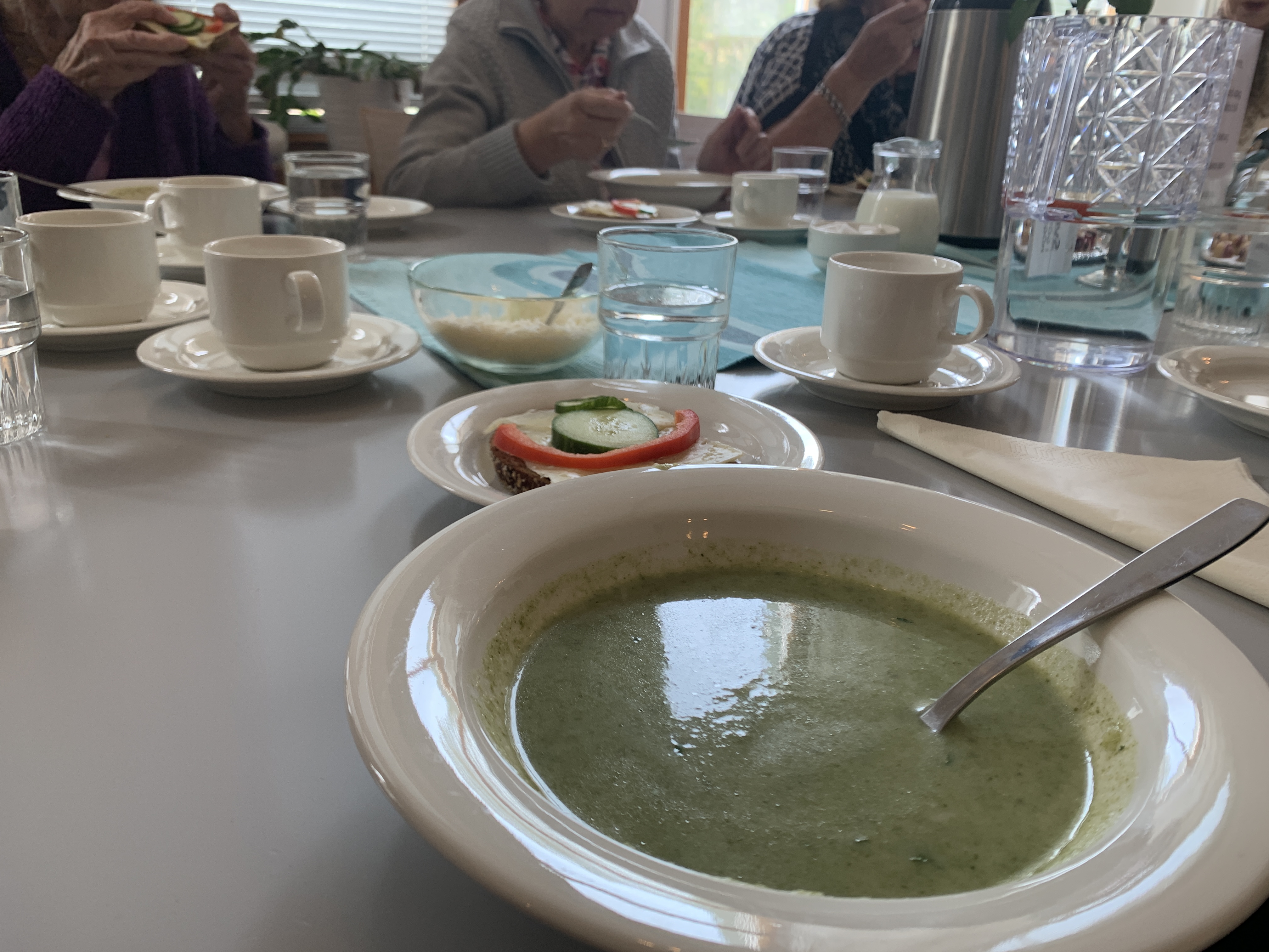 Soppa i tallrik, macka, samt människor i bakgrunden