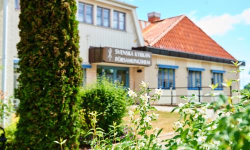 Träd och buskar i förgrunden. Svenska kyrkans församlingshem i bakgrunden.