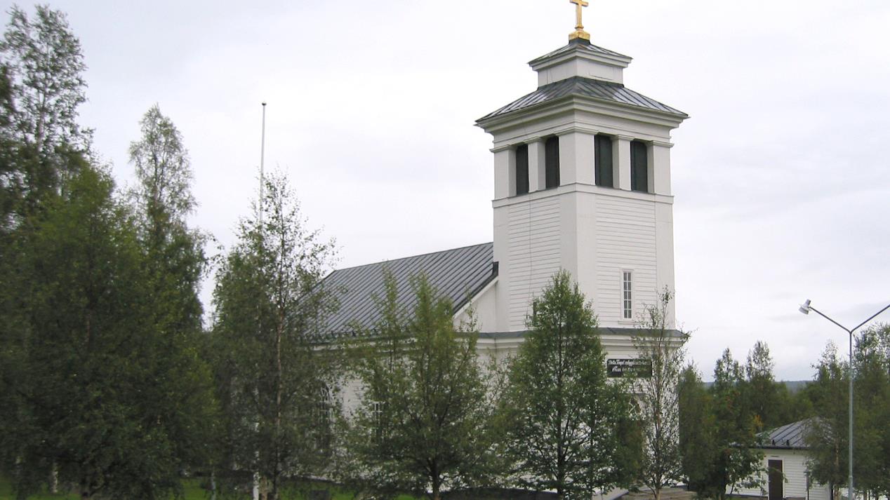 Tännäs kyrka med björkar och staket i förgrunden.