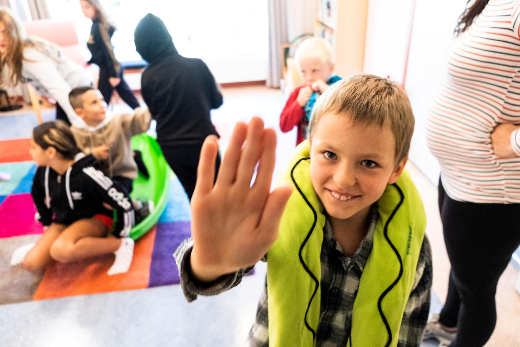 En pojke håller upp sin hand mot fotografen. Flera barn leker i bakgrunden.