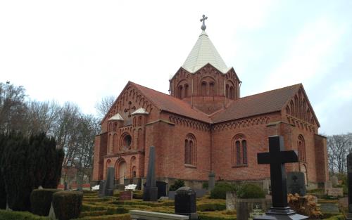 Korskyrka i röd tegel med torn i mitten av kyrkan.