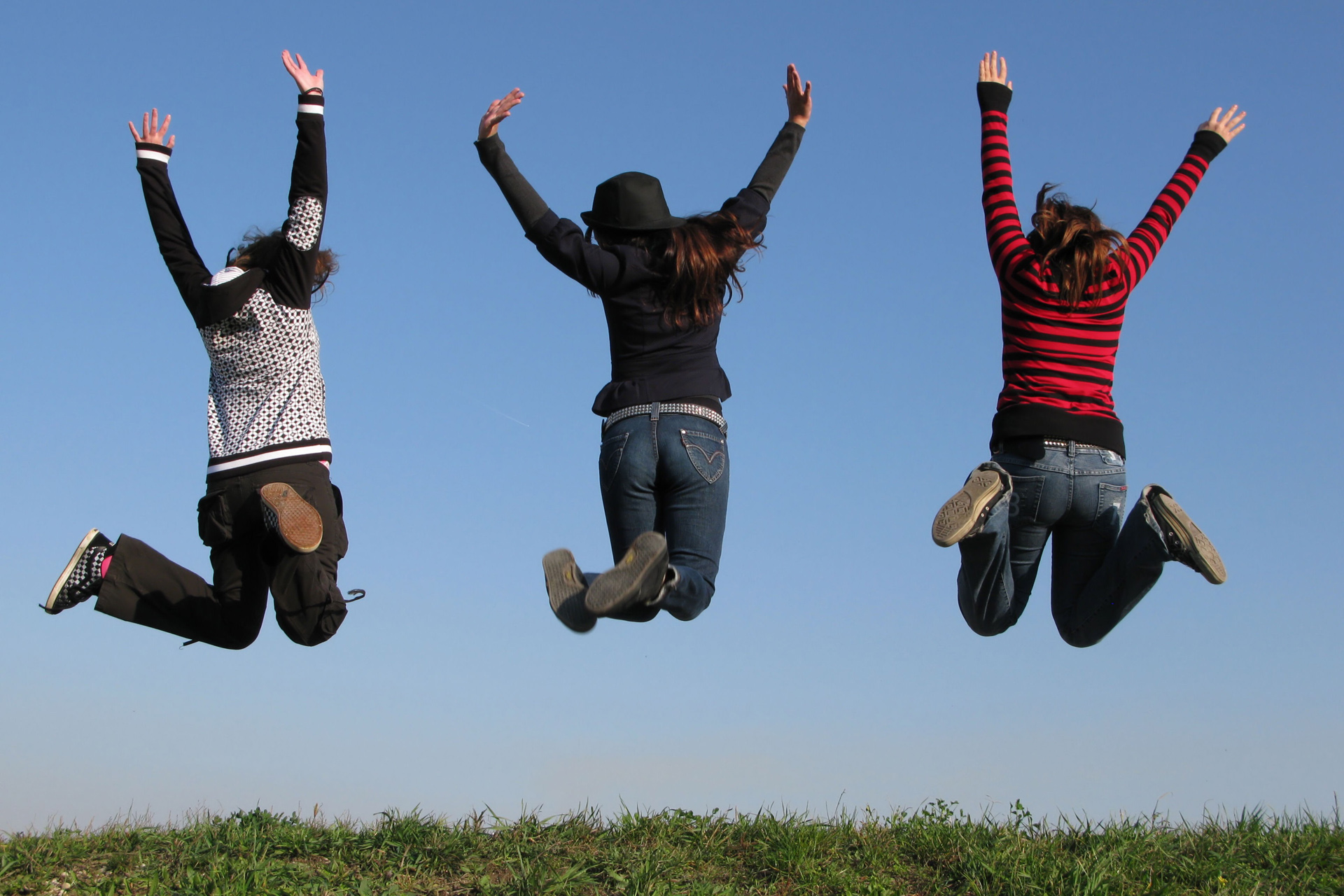 Unga personer hoppar upp i luften överst på en gräskulle.