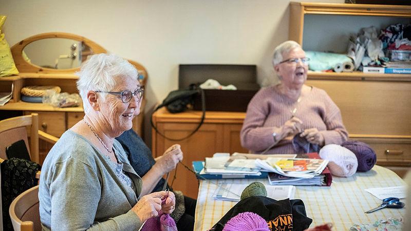 Glada äldre damer sitter och stickar och samtalar.