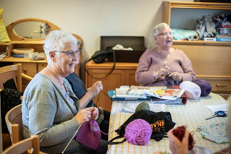 Glada äldre damer sitter och stickar och samtalar.