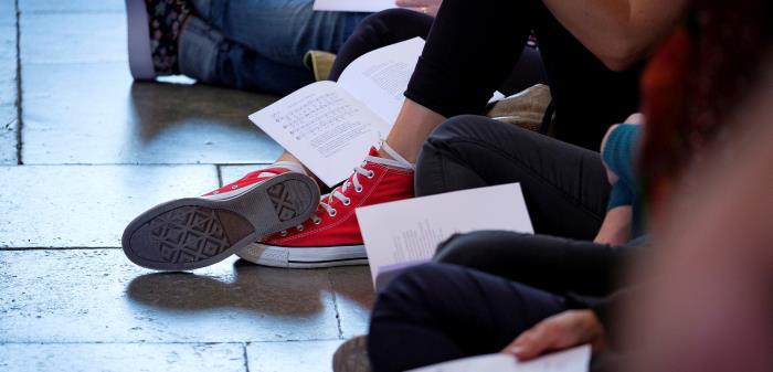 Unga människor sitter på golvet i korridor med sånghäften framför sig