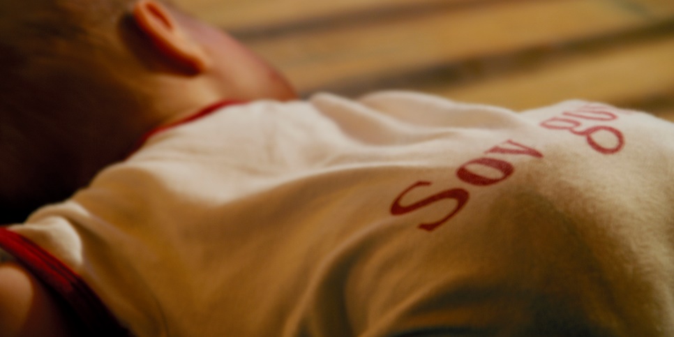 En bebis ligger på ett golv med huvudet vänt åt sidan. 