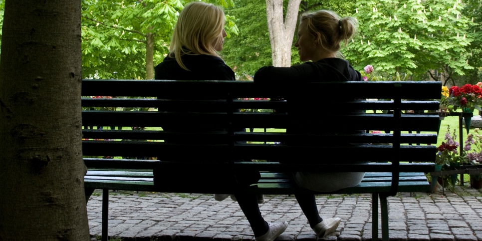 Två personer sitter på en parkbänk och samtalar