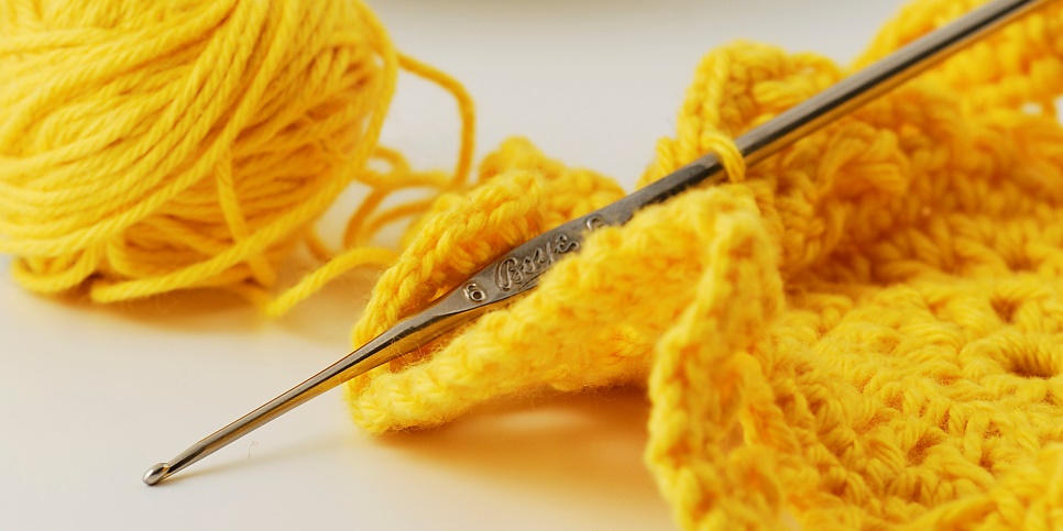 En gul trådrulle, en påbörjad stickning och en sticknål ligger på ett bord.