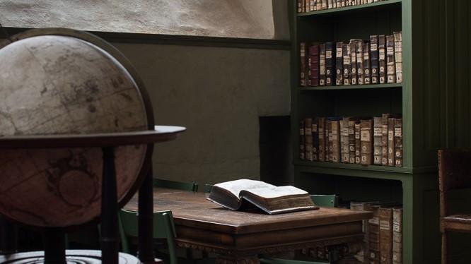 En gammal jordglob, en uppslagen bok på ett bord och en bokhylla i Domkyrkobiblioteket.
