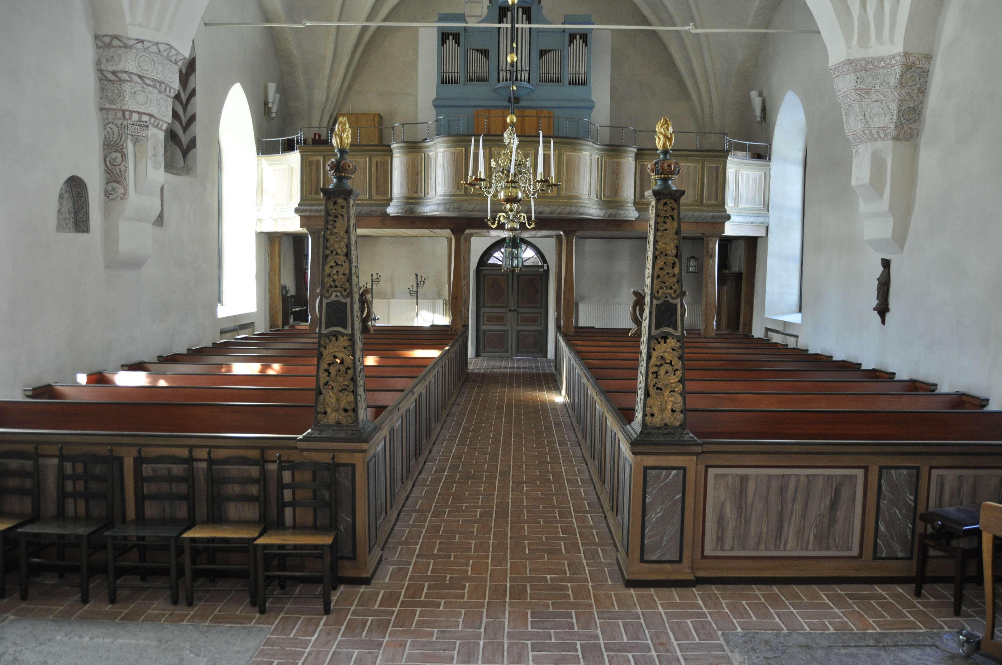 Enåkers kyrka invändigt med stängda träbänkar, utsirade pelare, tegelgolv och vitkalkade väggar.