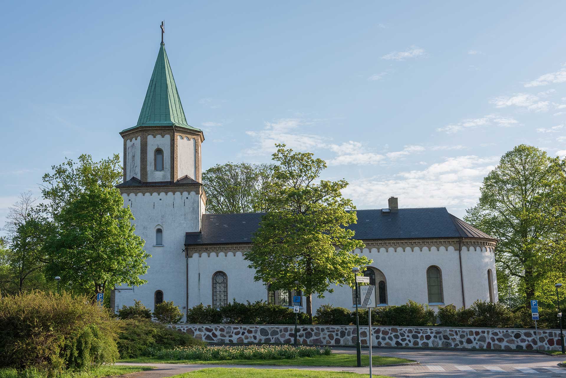 Vitkalkad kyrka med torn omgärdat av gröna träd