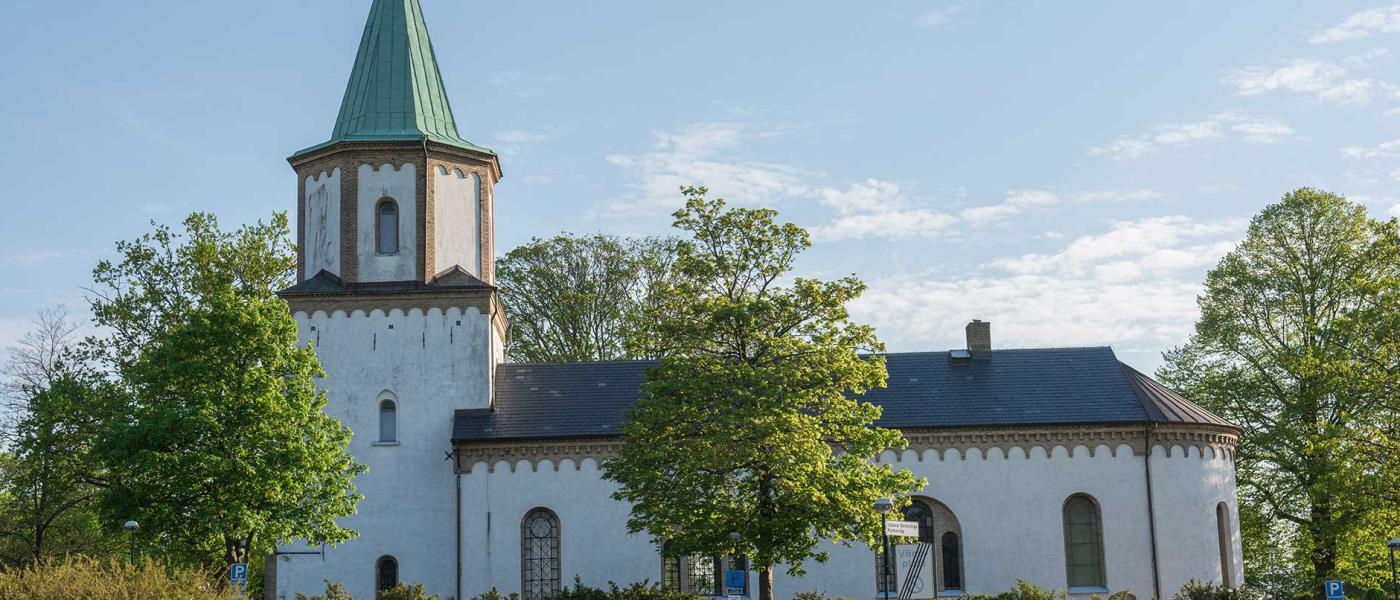 Vitkalkad kyrka med torn omgärdat av gröna träd