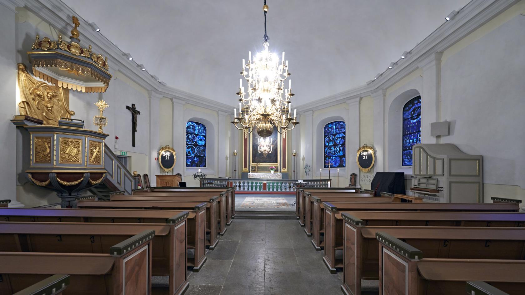 Mjölby kyrka invändigt. Altargången med kyrkbänkar. Till vänster syns predikstolen och längst fram altaret.