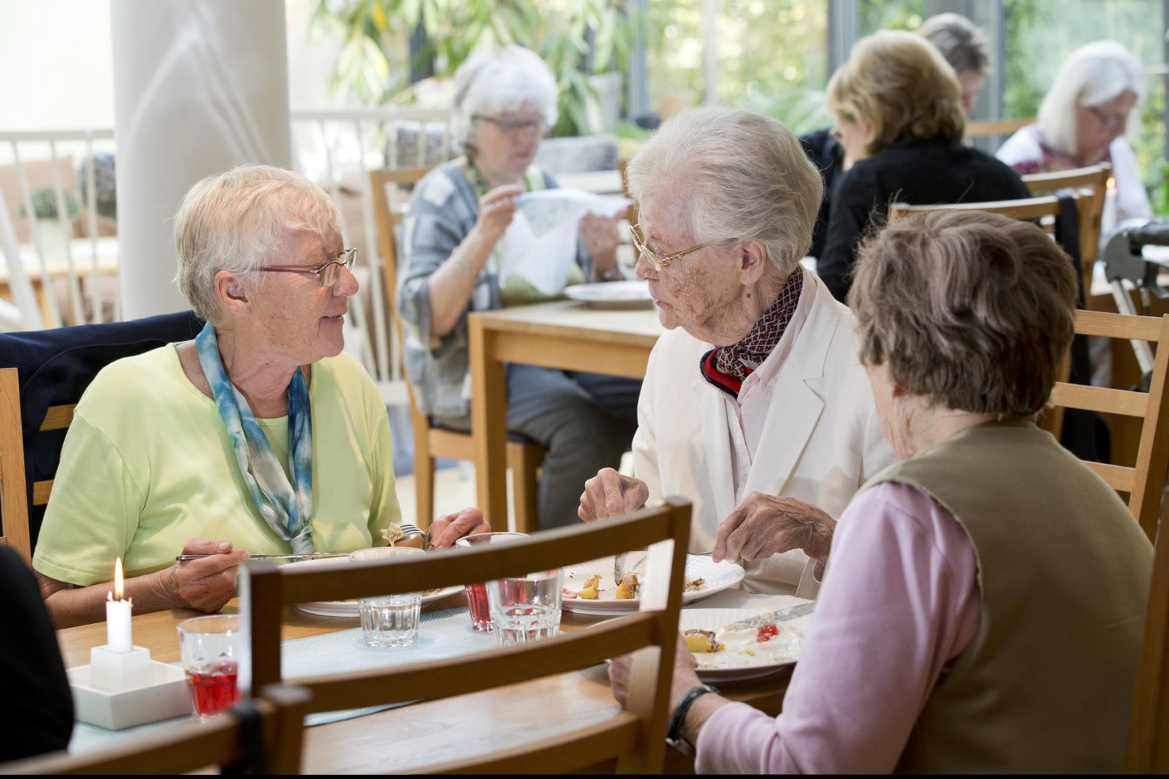 Bilden visar tre äldre kvinnor som äter lunch i Laurentiusgårdens matsal. 