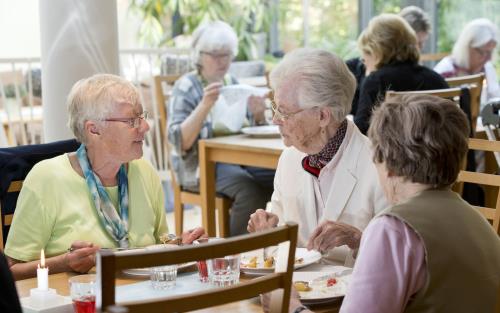 Bilden visar tre äldre kvinnor som äter lunch i Laurentiusgårdens matsal. 