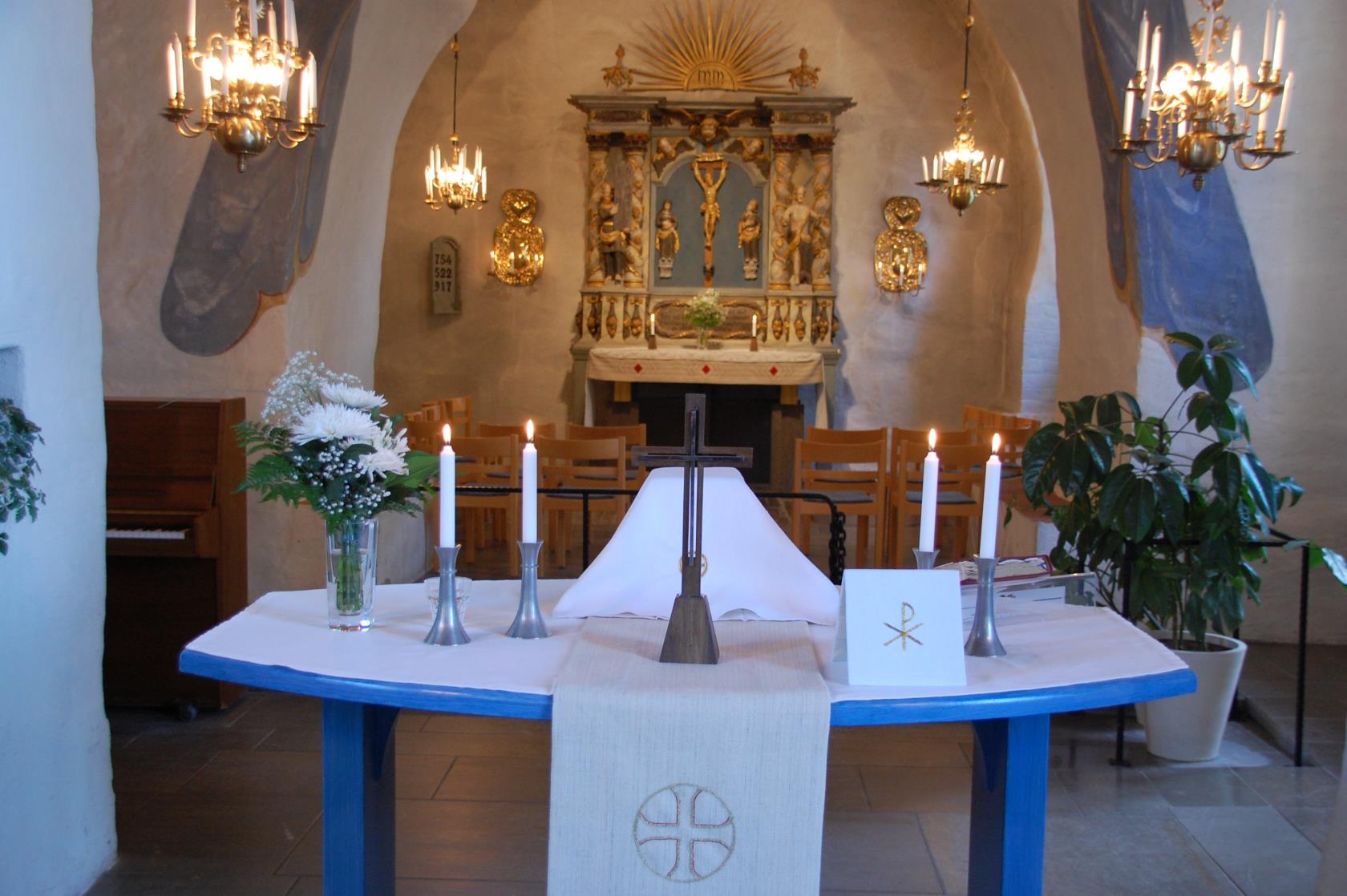 Dukat altarbord i Ödeshögs kyrka. Den liturgiska färgen är vit och på altaret står ett kors, fyra ljus och en vas med vita blommor.