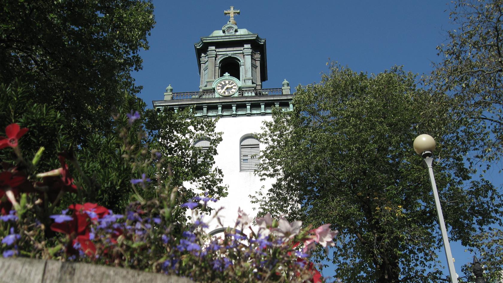 Carl Johans kyrka på sommaren. Framför kyrkan blommar blå och röda blommor.