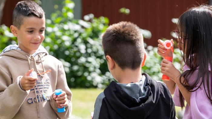 Tre barn blåser såpbubblor tillsammans.