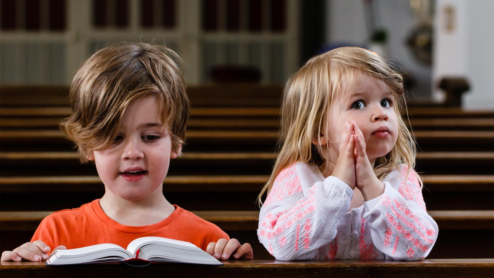 Två barn sitter i kyrkbänkar. Det är en bok framför det ena barnet. 