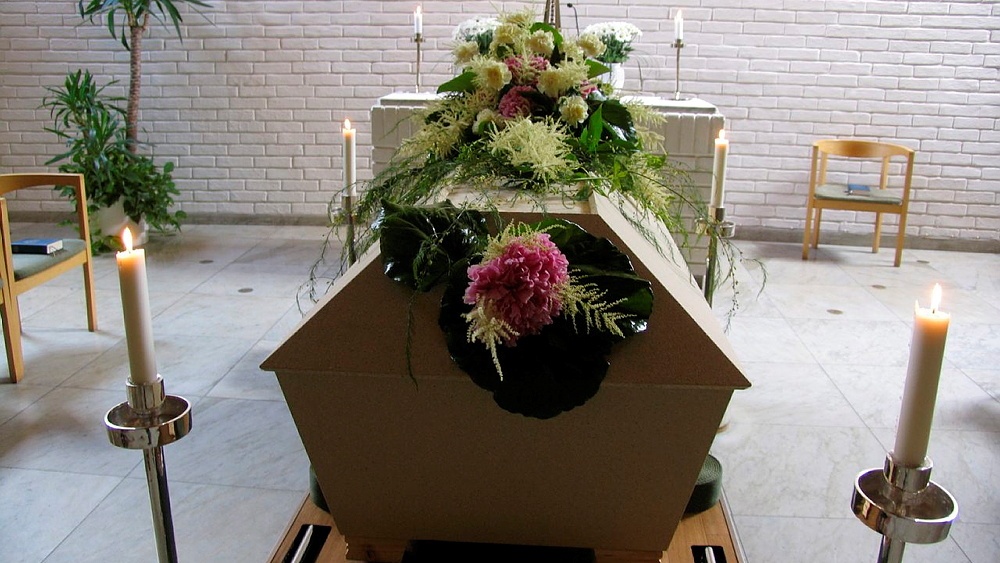 Blomstersmyckad kista och levande ljus i kyrkorum.