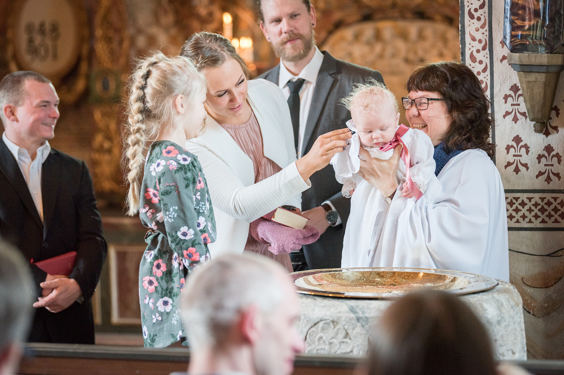 En familj och en präst framme vid dopfunten under ett dop.