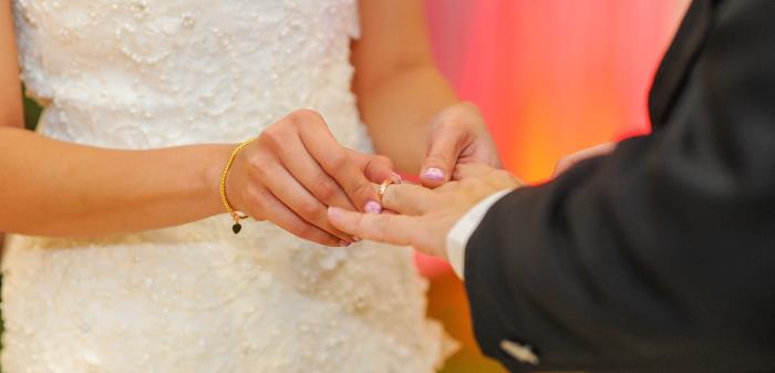 Händer av ett bröllopspar, den ena sätter en ring på den andres ringfinger