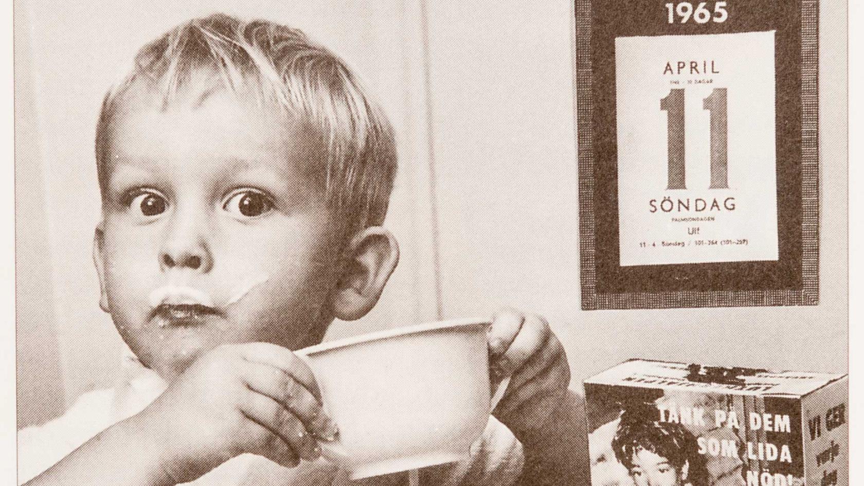 Äldre bild på liten pojke som äter frukost och det står en fastebössa på bordet. 