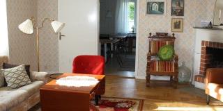 En soffa, några stolar, en öppen spis, några tavlor på en vägg, en lampa, parkettgolv - Frösundagårdens soffrum 