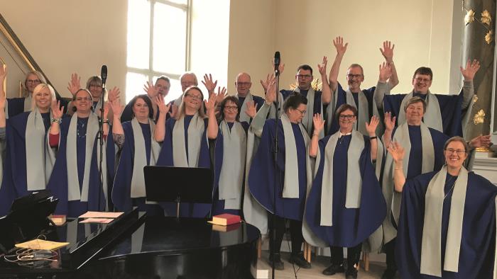 Glad gospelkör med händerna i luften, i kyrka