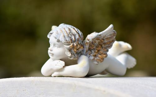 Vit ängel med guldfärg på hår och vingar vilar på gravsten.