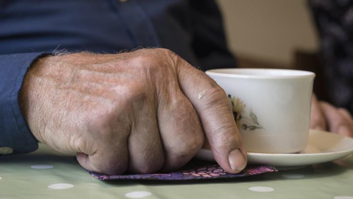 En äldre mans hand som vilar vid en kaffekopp.