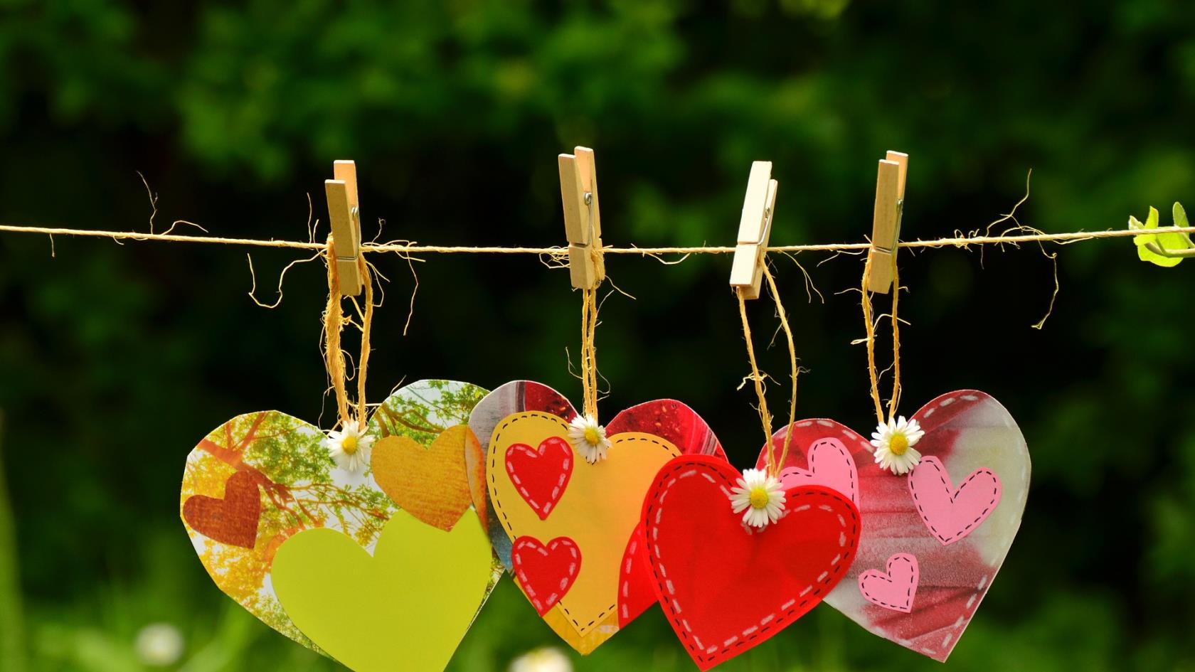 Fyra klädnypor med varsitt färgglatt hjärta upphängda på ett snöre.  