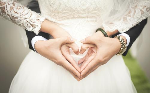 Två par händer omsluter varandra och formar ett hjärta framför en brudklädd person.