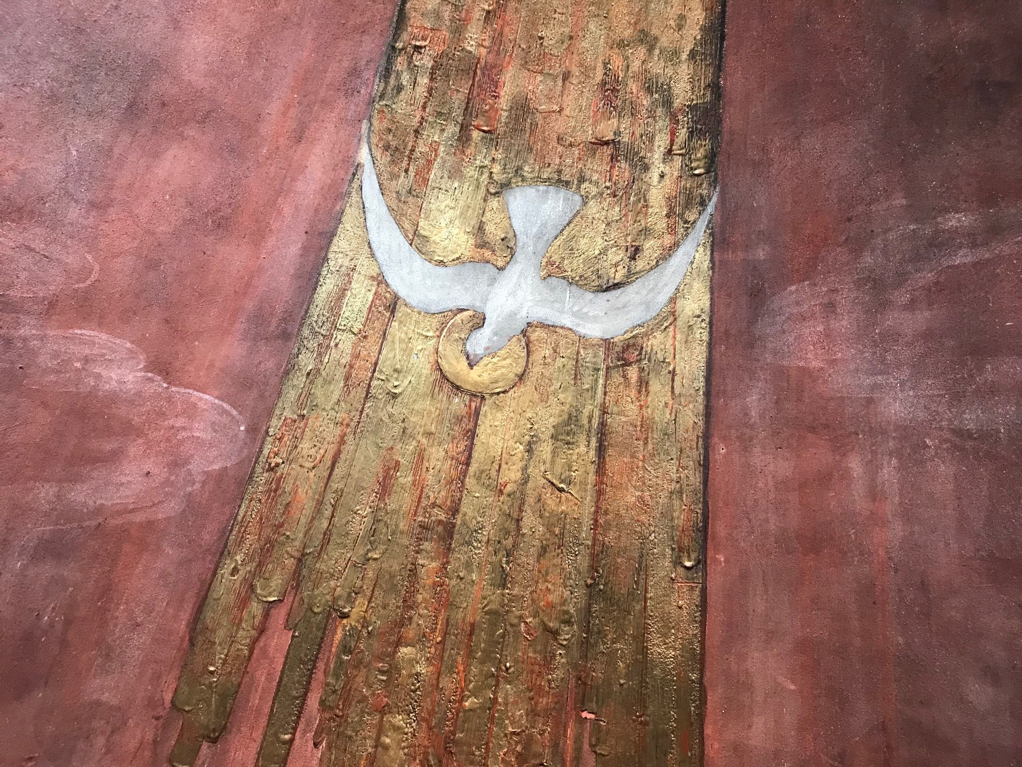 Målning i Klosterkyrkans dopkapell. En vinröd bakgrund. En duva som symboliserar den helige ande är målad i ett stråk av guld.