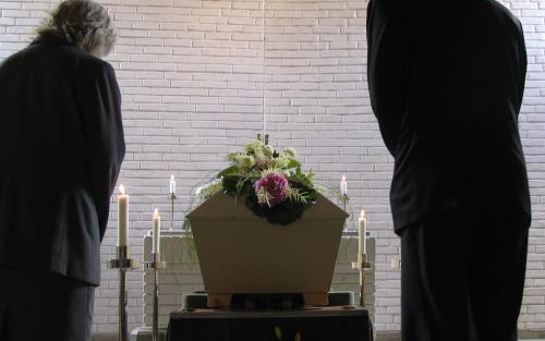 En man och en kvinna bugar framme vid kistan under en begravning.