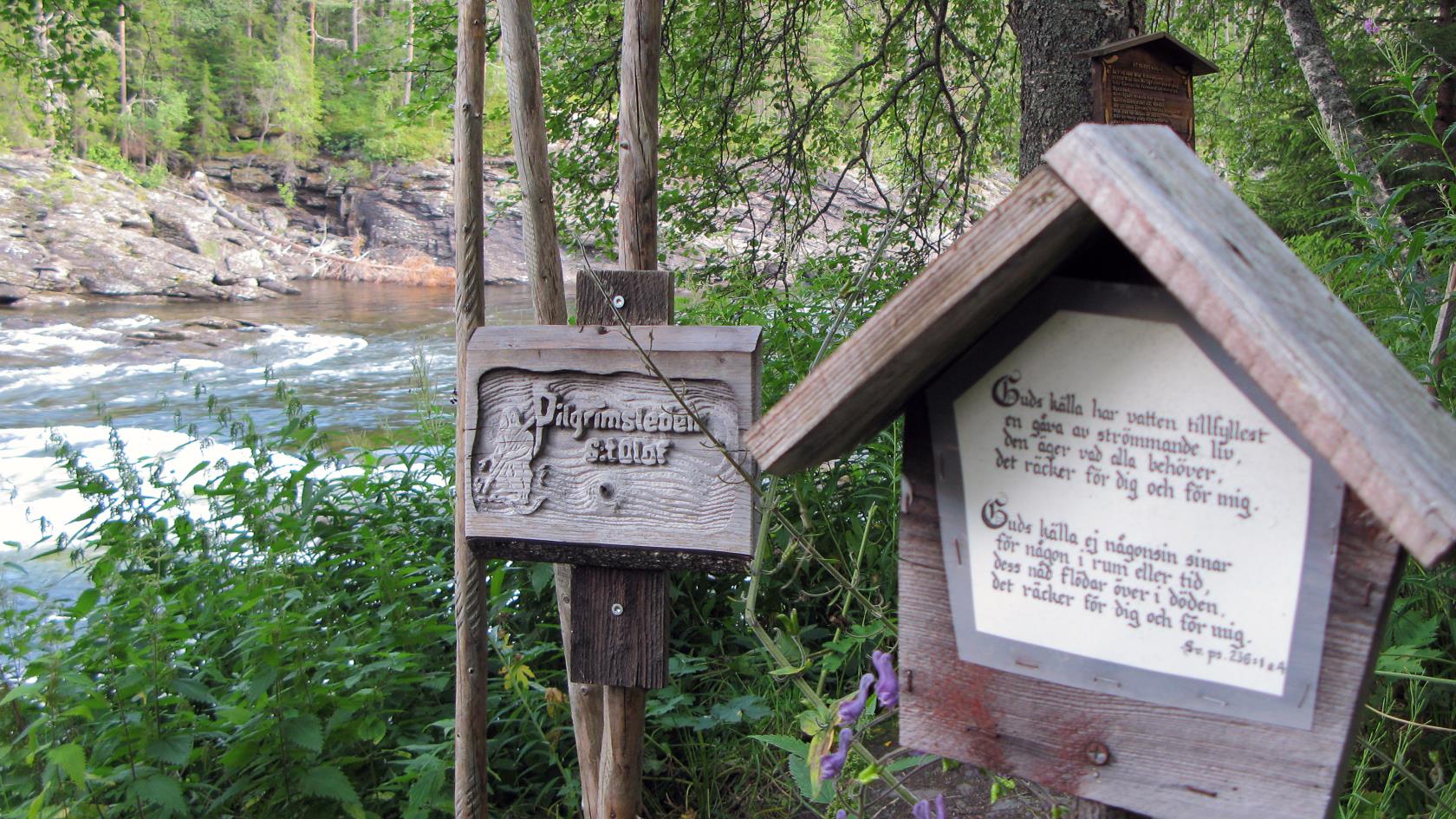 På en snidad träskylt vid en fors står det Pilgrimsleden S:t Olof.