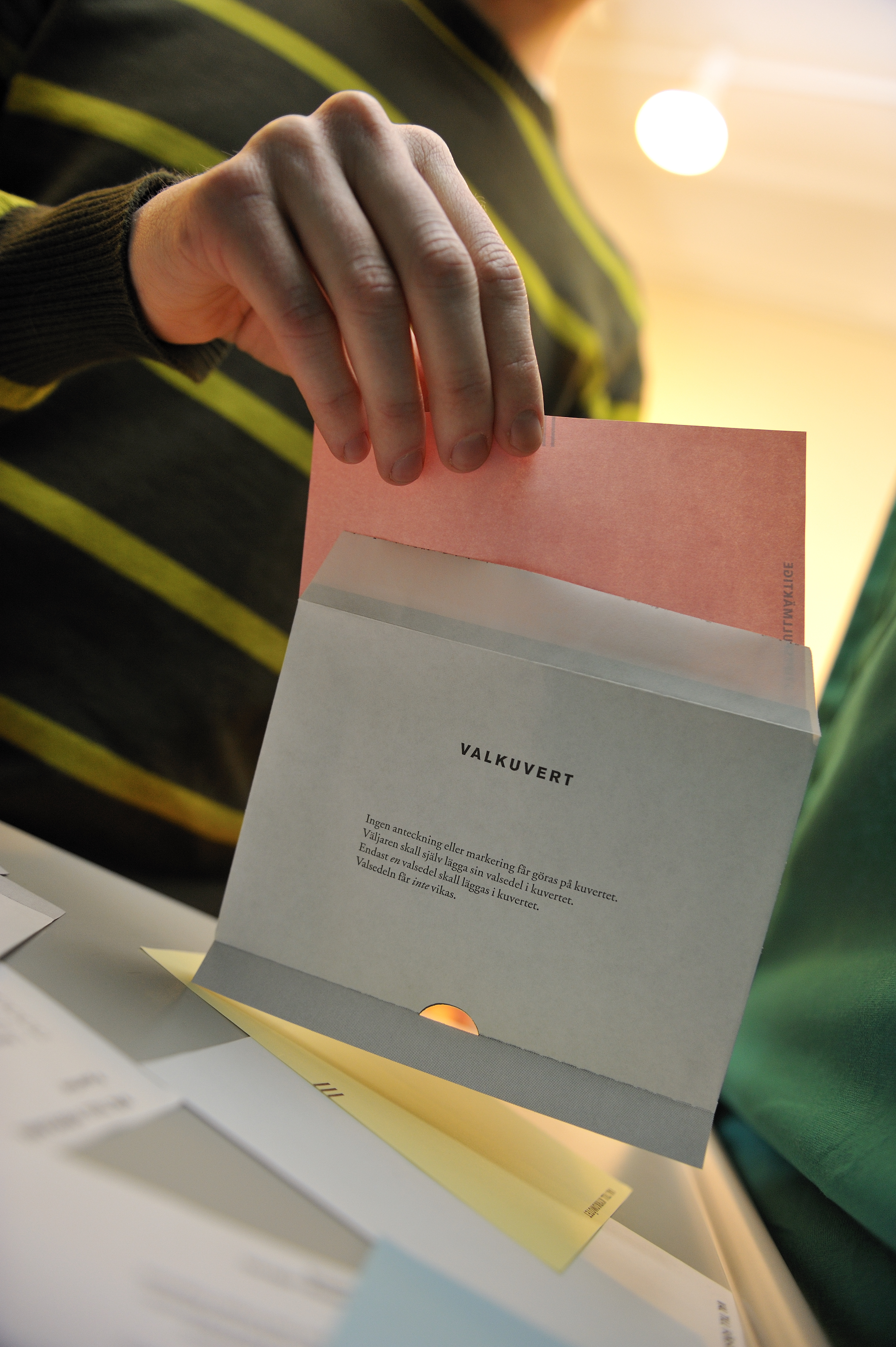Någon stoppar en rosa valsedel i valkuvertet.