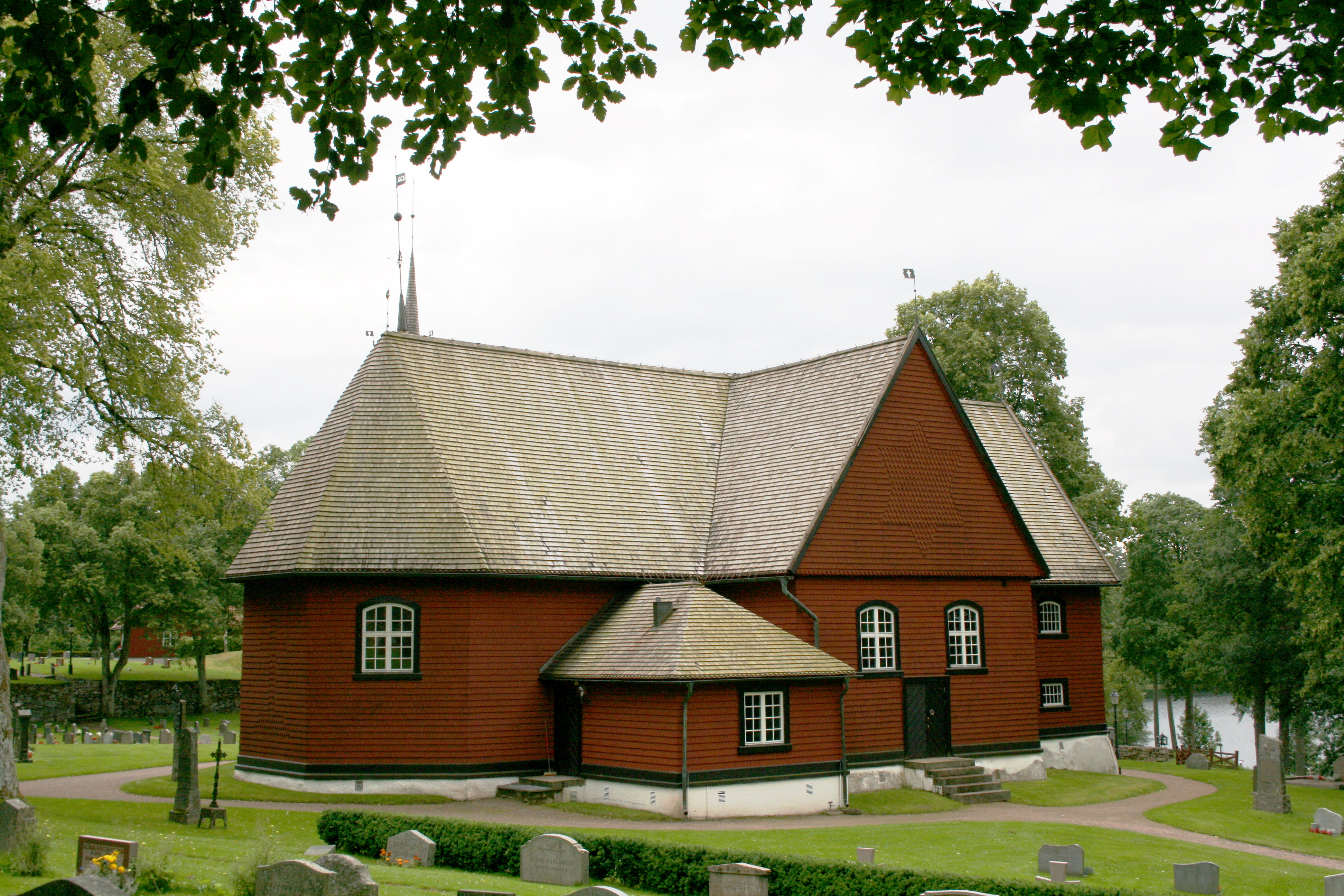 En röd träkyrka. Trädkronor i förgrunden.