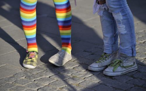 Två barn står bredvid varandra, bara benen syns. Den ena har regnbågsfärgade strumpbyxor.