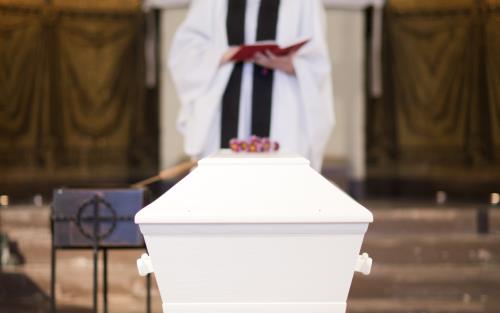 En präst står bakom en vit kista inne i en kyrka.