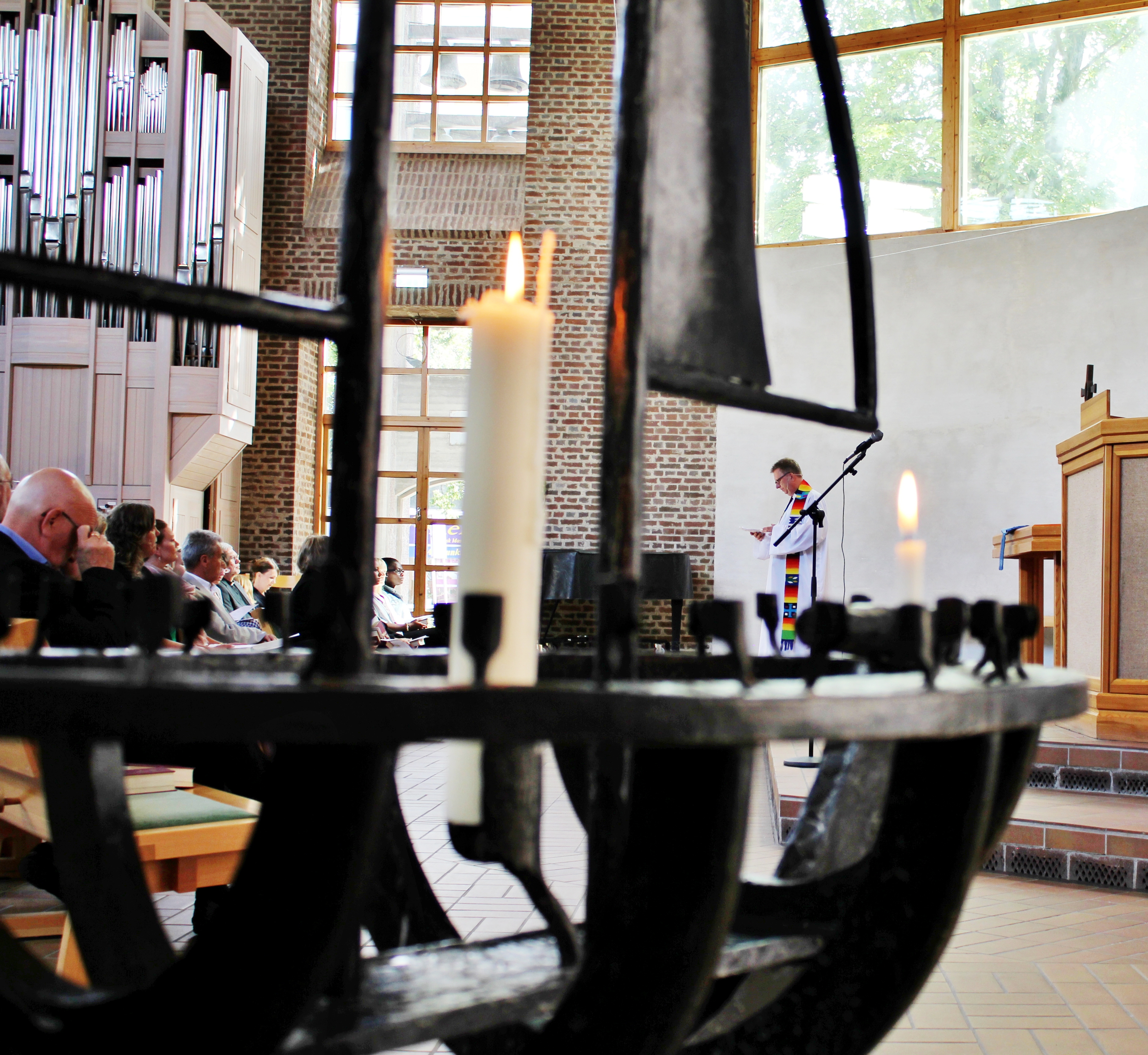 Bortom en stor ljusbärare i smitt järn står en präst och talar till församlingen.