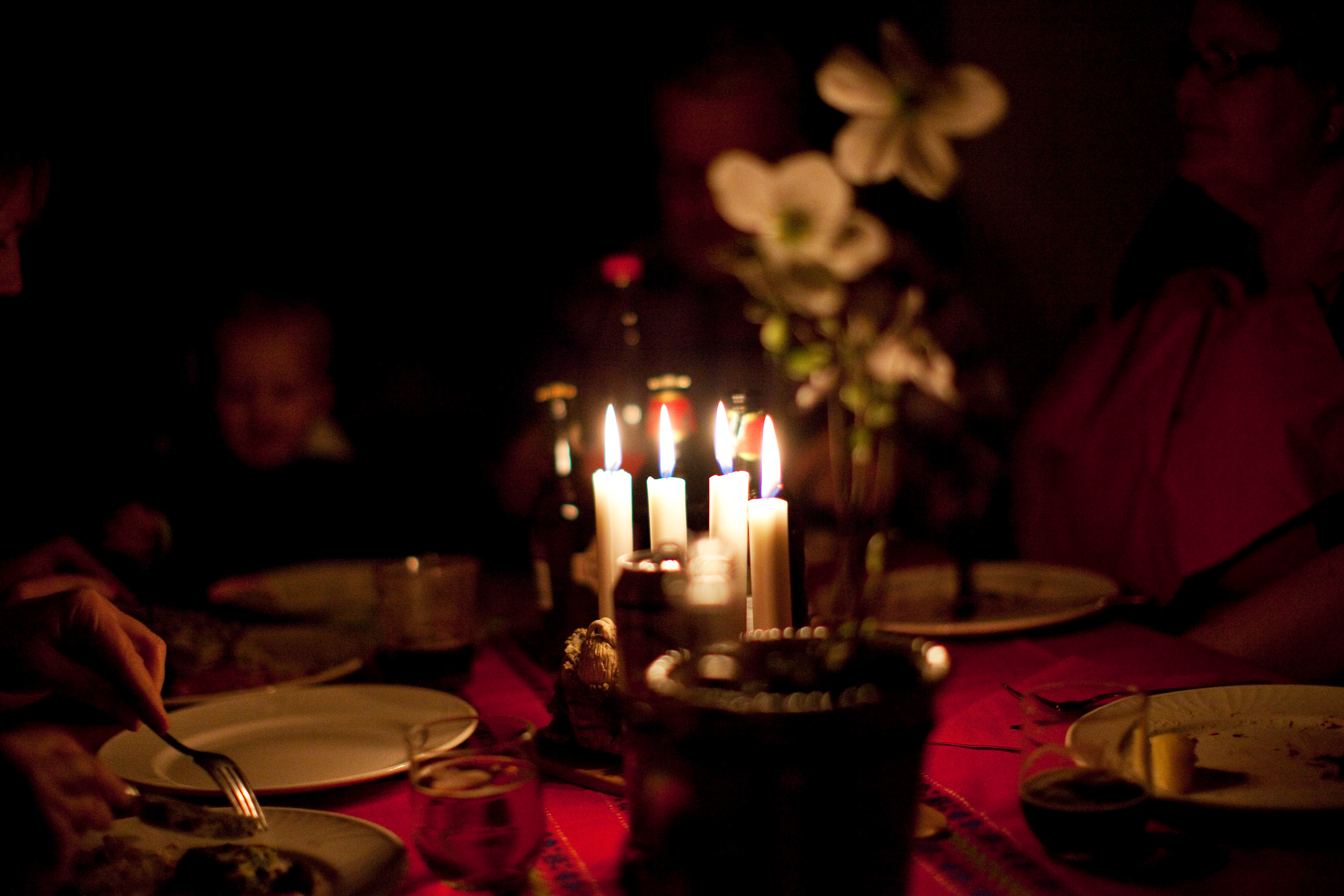 Några vuxna och barn sitter runt ett julbord. En adventsljusstake med fyra ljus tända står på bordet.