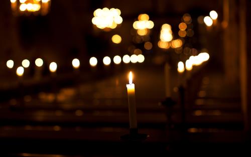 Suddig bild av tända ljus som lyser i en mörk kyrka.