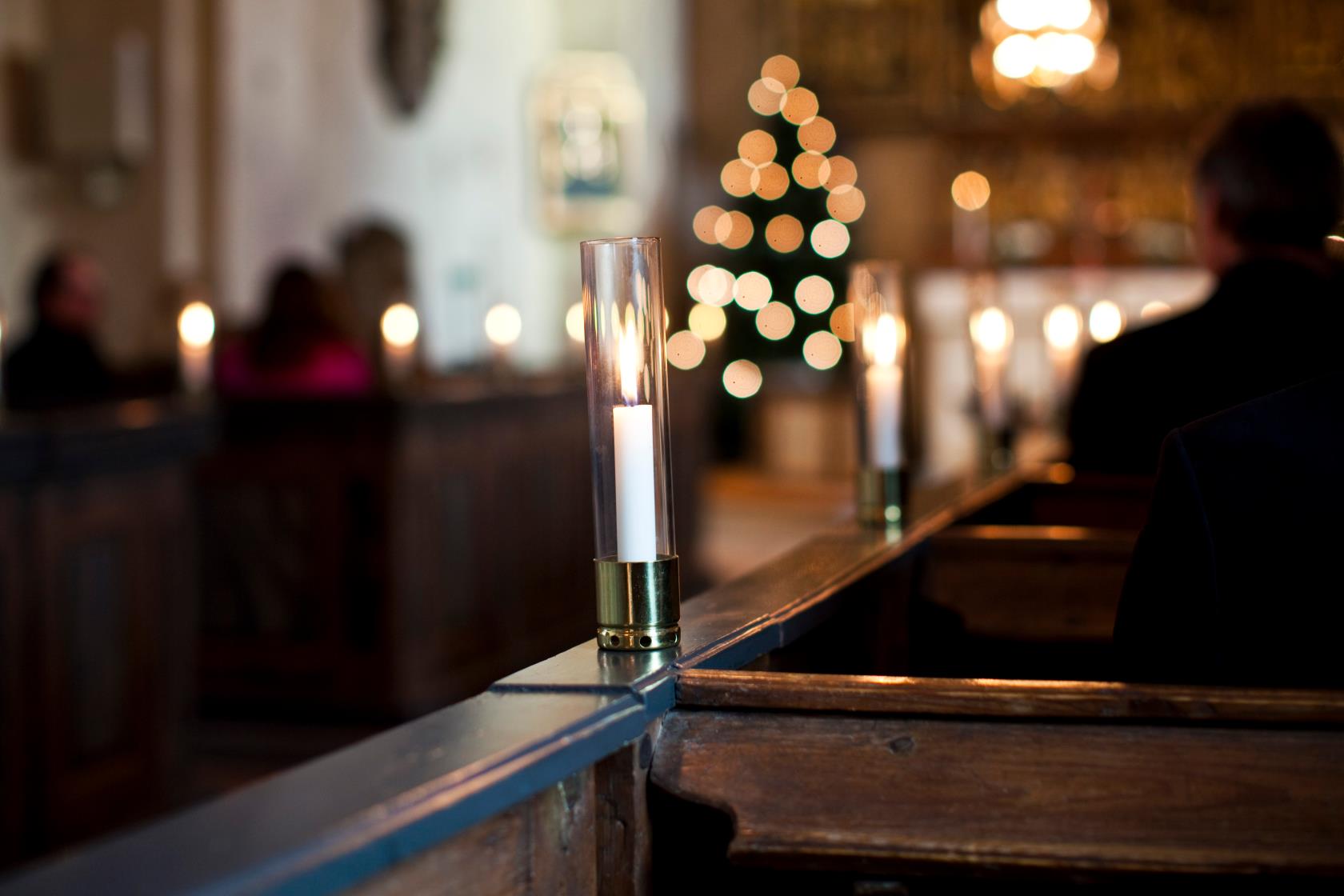 Tända ljus i glasrör står på varje bänkrad i en kyrka.